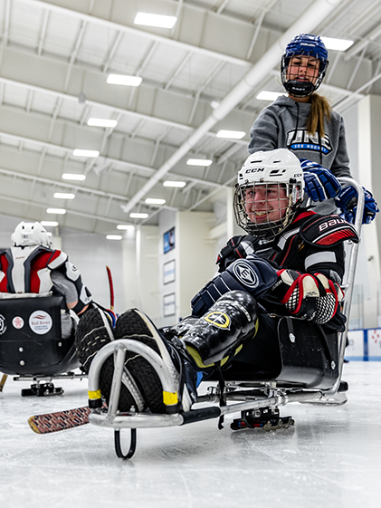A UNE physical therapy student guides a man on an adaptive sled.