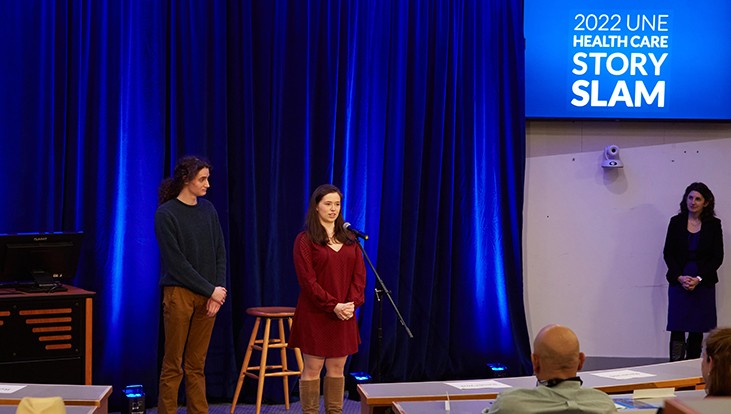 Two presenters stand on a stage at U N E's healthcare story slam event