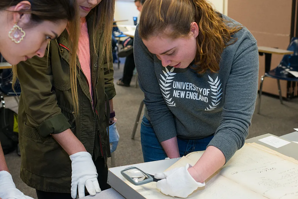 Students using a magnifying glass to look at historical U N E documents