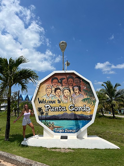 Ana Maria Castellanos poses in front of a sign welcoming visitors to Punta Gorda