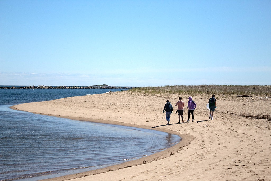Four U N E students walking down the beach next to the ocean
