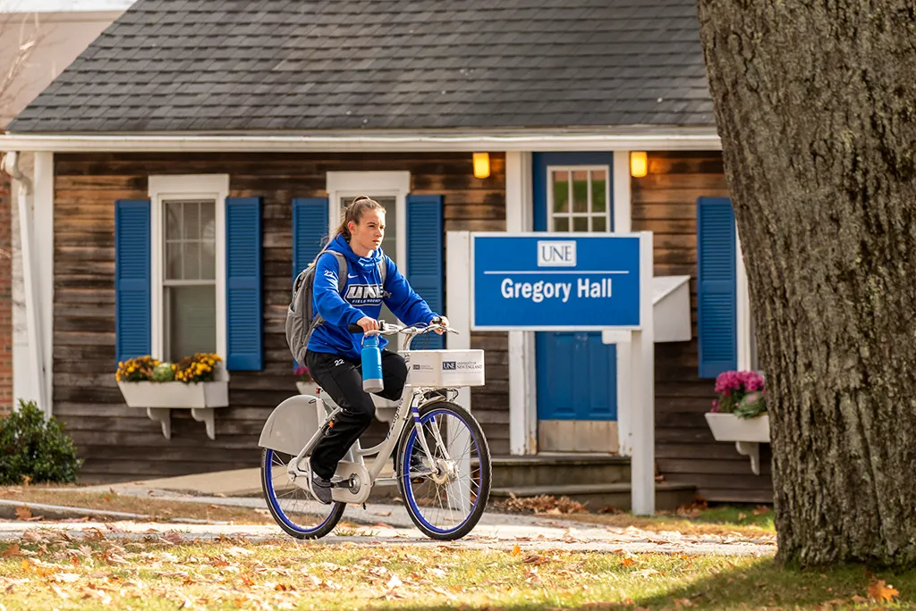 A U N E student riding a bicycle through Biddeford Campus
