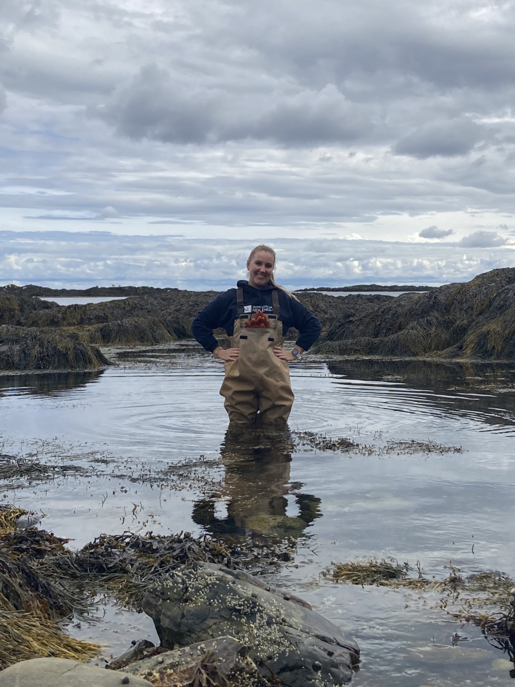 U N E student Melissa Butler stands in a tide pool wearing waiters