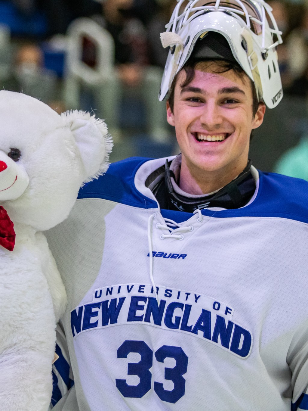 A men's hockey player smiles while holding a teddy bear at the 2022 Teddy Bear Toss at the Harold Alfond Forum
