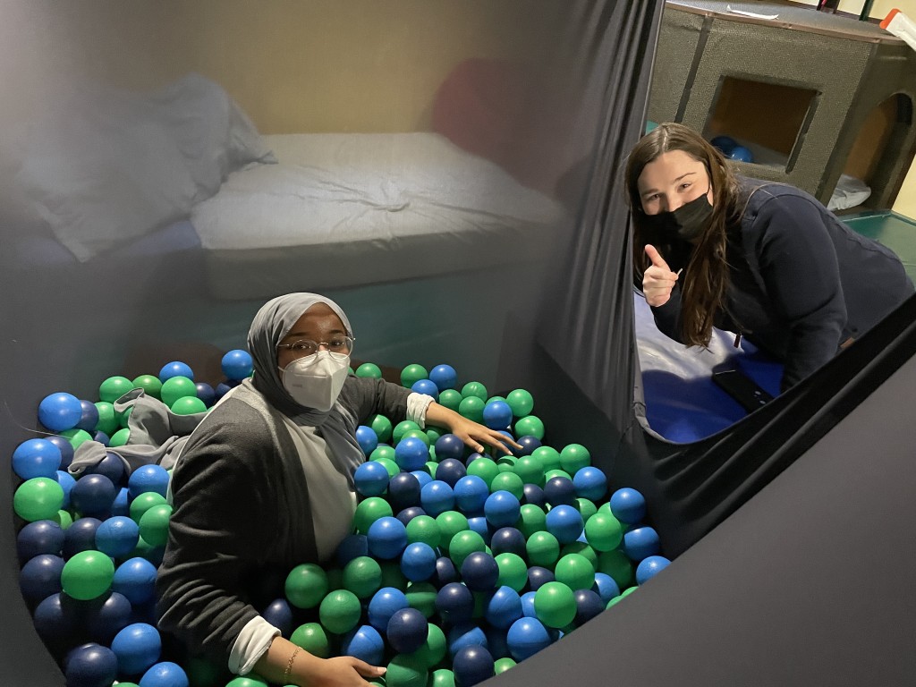 Two female students; one sits in a ball pit