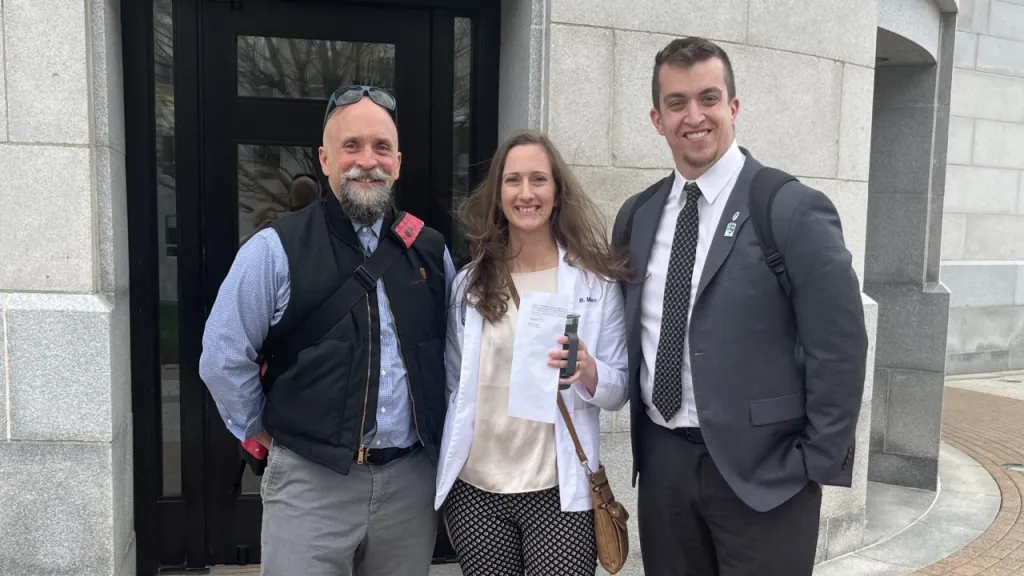 Ed Cervone, Bethany Miles, and Austin Vaughan pose in front of the Maine State House