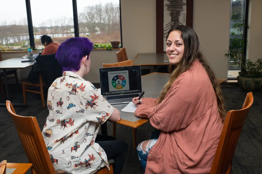 Two students study at a table with a lap top