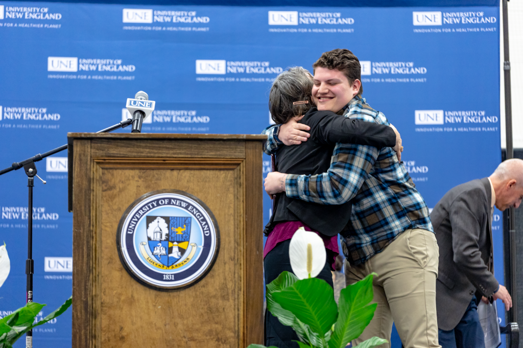 student and faculty hugging on stage