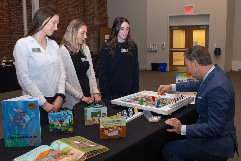 Three female students demonstrate their adaptive board games for UNE President Herbert