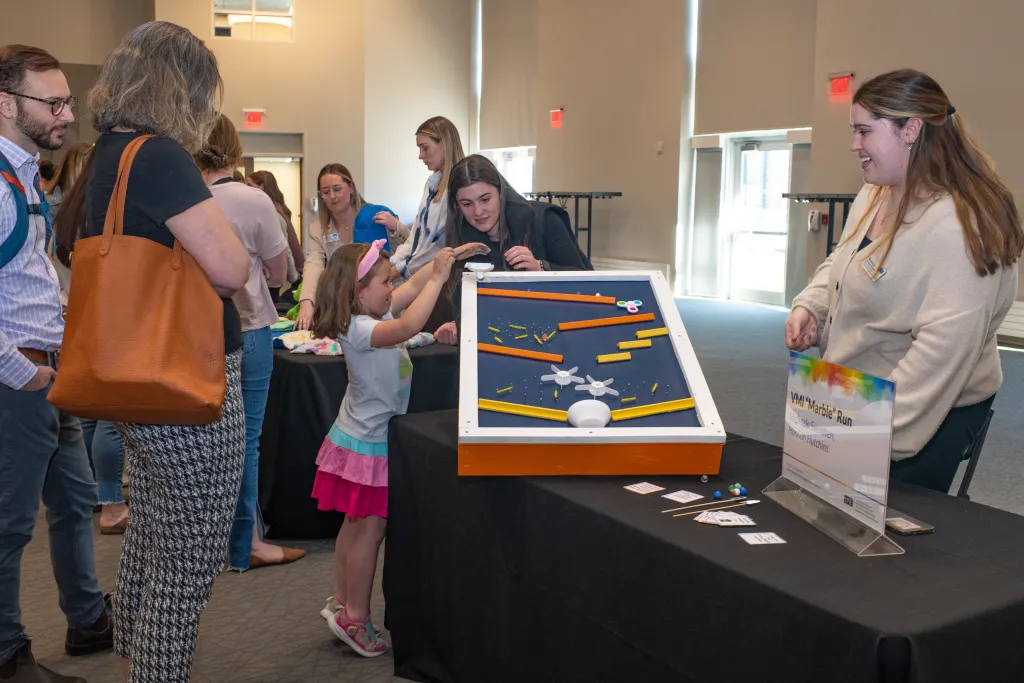 Students instruct a child how tp play with the marble run they built by hand