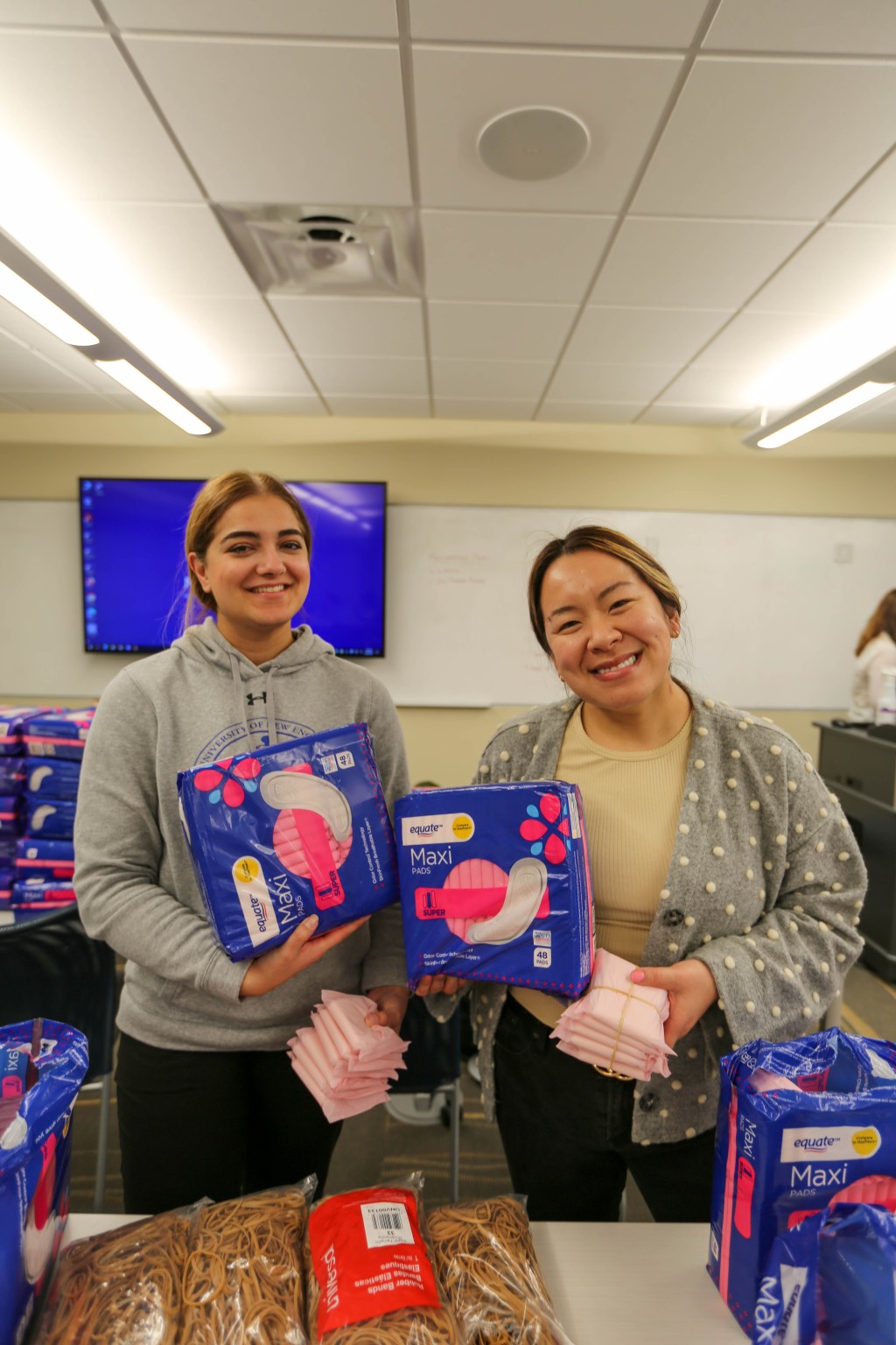 two students holding bags of menstrual pads and smiling