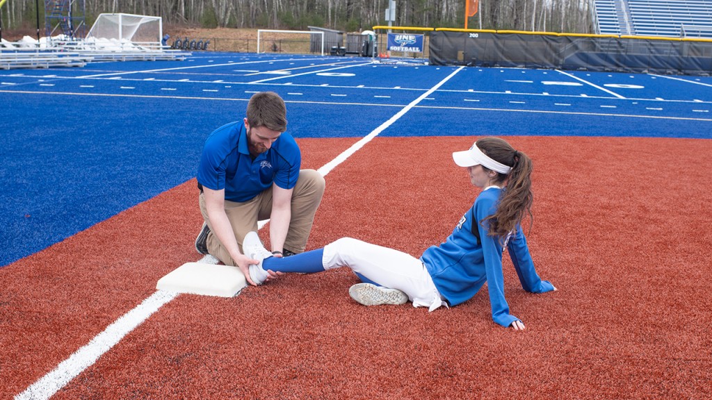 A student checks the ankle of a U N E softball player