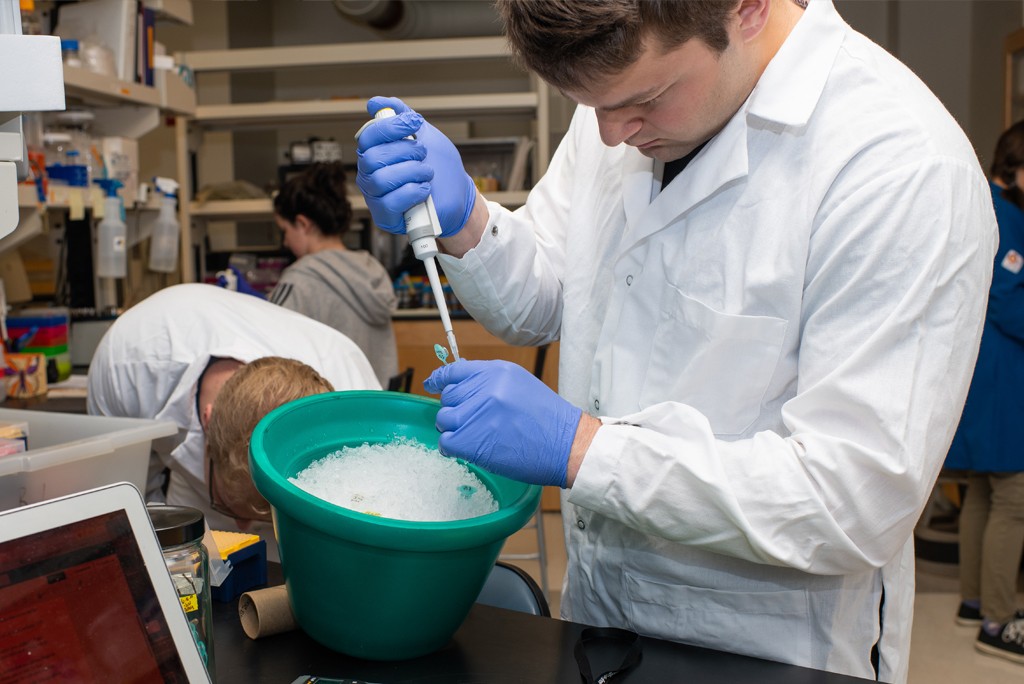 A student wears white coat while working with lab tools