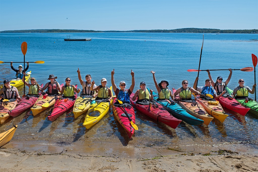 A group of students sitting in kayaks on the shore