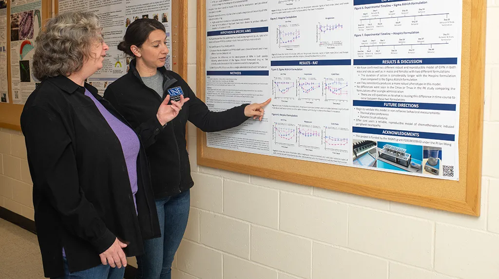 A student presents their research poster to a faculty member