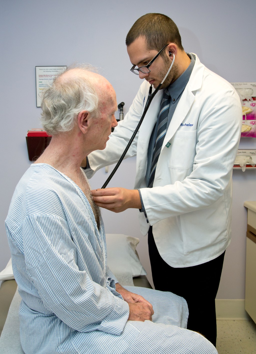 A C O M student uses a stethoscope to listen to an elderly patient's heartbeat and breathing