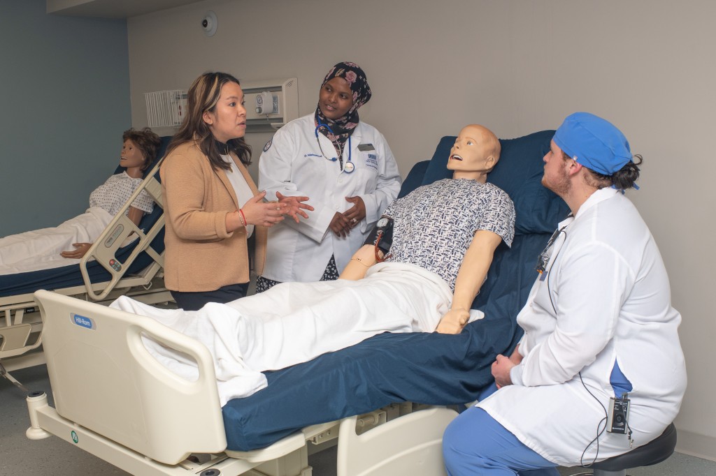 A group of health students discuss treatment for a patient dummy in the Simulation Lab