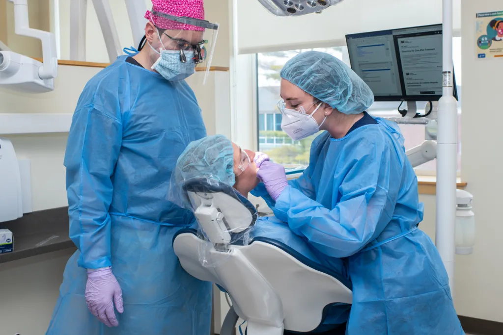 A dental student and a physician assistant student look into the mouth of a patient during a dental screening