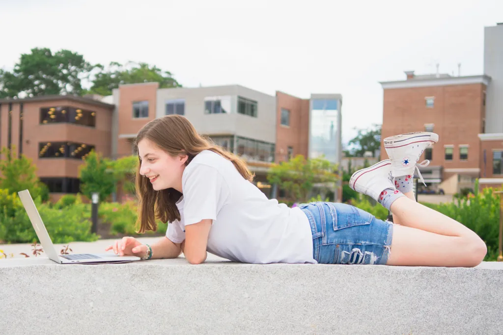 A student using their laptop while laying outside