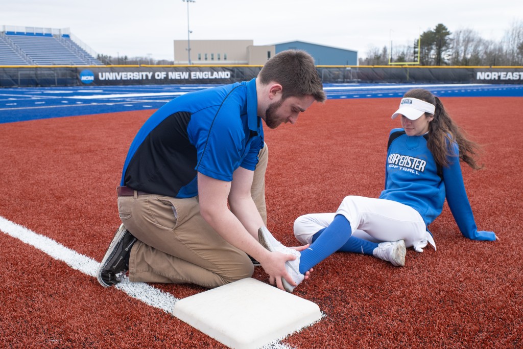 An athletic training student assists a baseball player out on the field