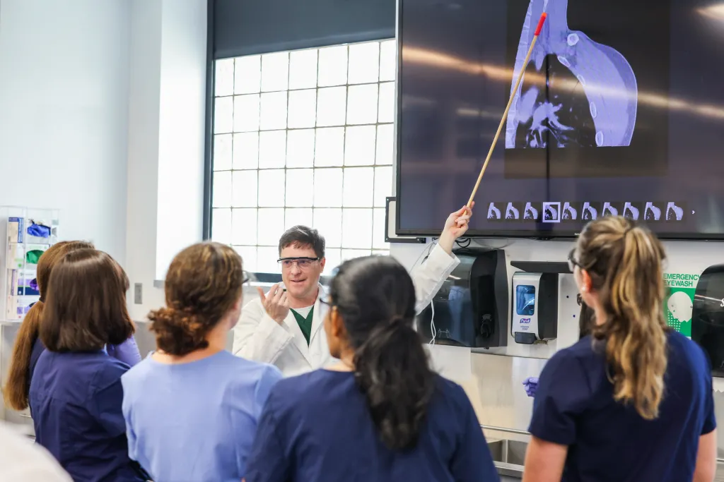 A professor points to a screen as he describes the visuals to a group of anatomy students