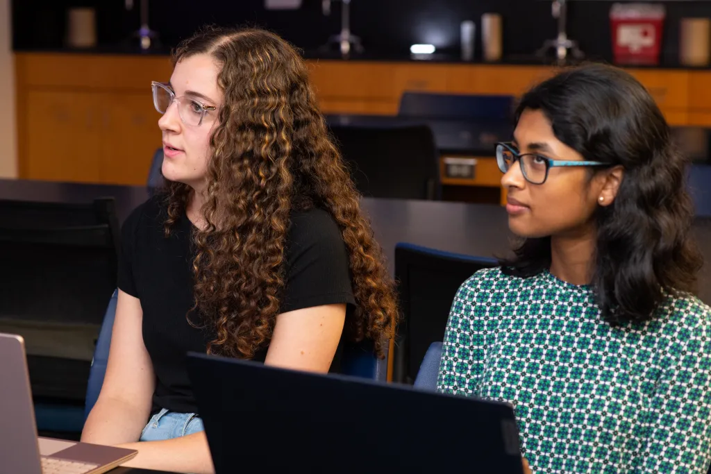 Two anatomy students listen to a lecture while taking notes on their laptops