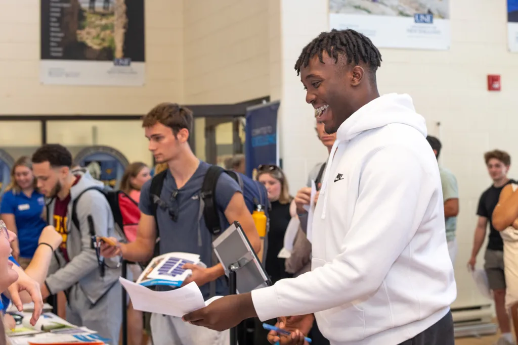 A student smiles as they hand in forms at an orientation event