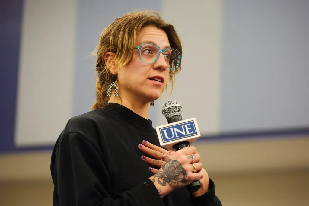 A woman speaks into a U N E-branded microphone at a President's Forum event