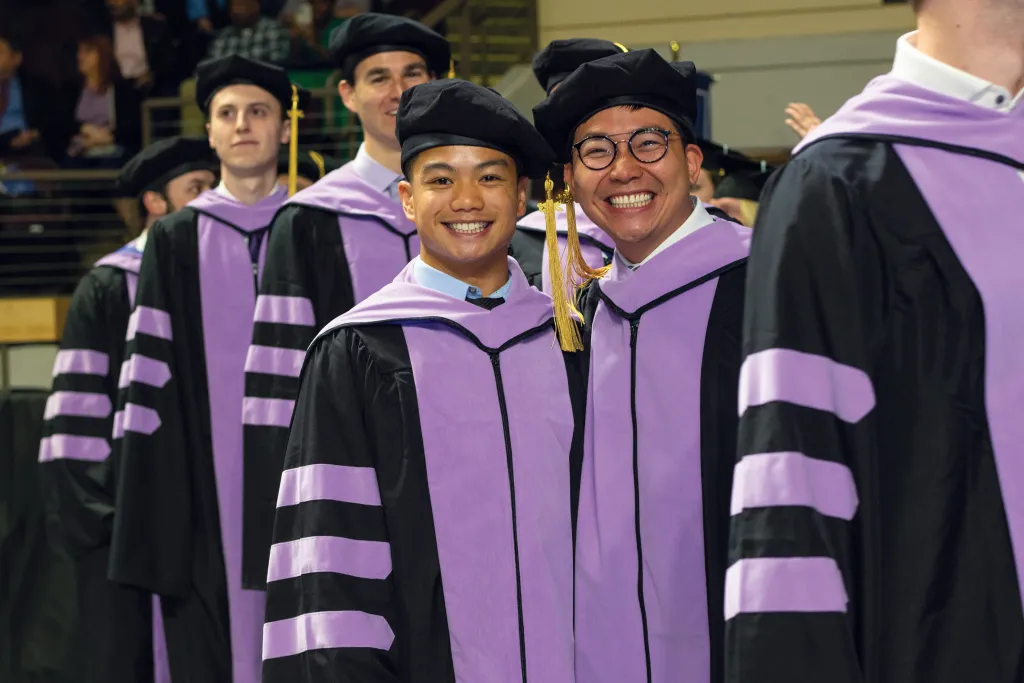 Two students stand in like to walk across the stage at the 2023 U N E commencement ceremony