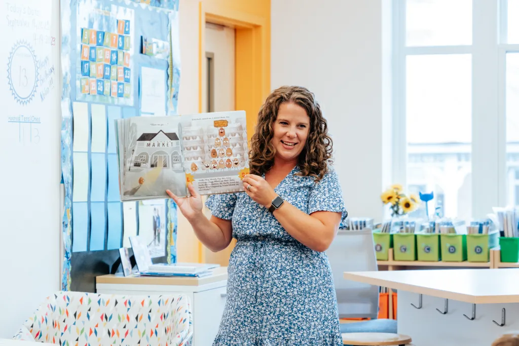 Emily holds up a children's book in front of her classroom