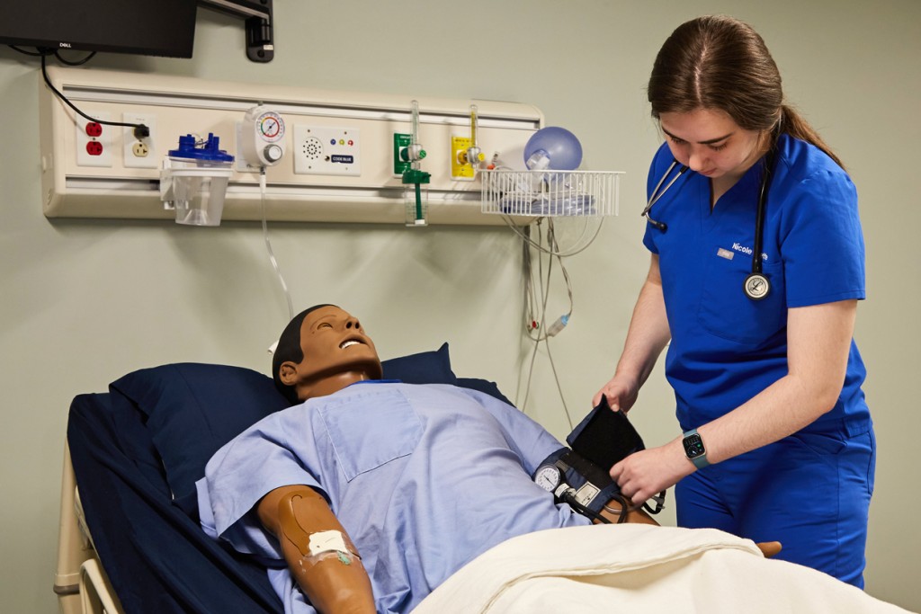 A physician assistant student practices taking blood pressure on a patient simulator