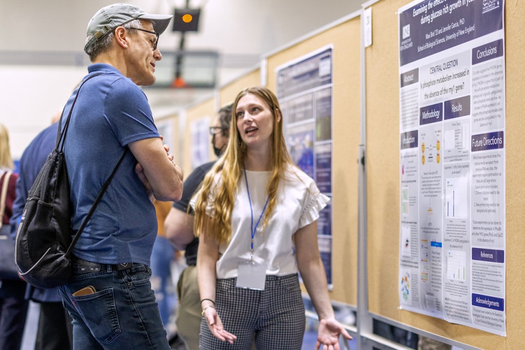 A student describes their research poster to an audience member at an Undergraduate Research Symposium