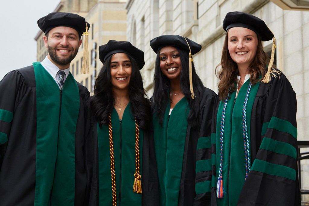 Four C O M students in their green and black academic regalia prior to their graduation ceremony