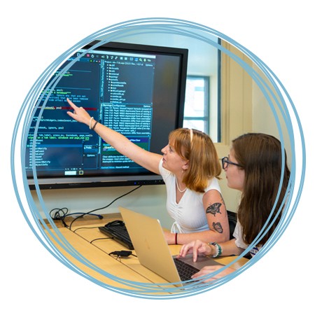 Two students review computer programming code on a large monitor