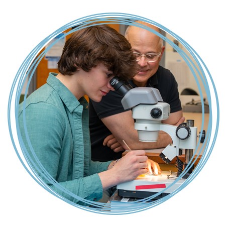 A faculty member assists a student with looking into a microscope