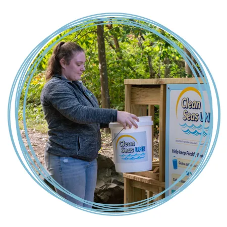 A student brings a filled Clean Seas U N E bucket to the drop-off location on the Biddeford Campus