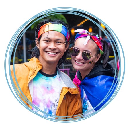 Two U N E students wearing rainbow headbands and smile at a Portland Pride Parade