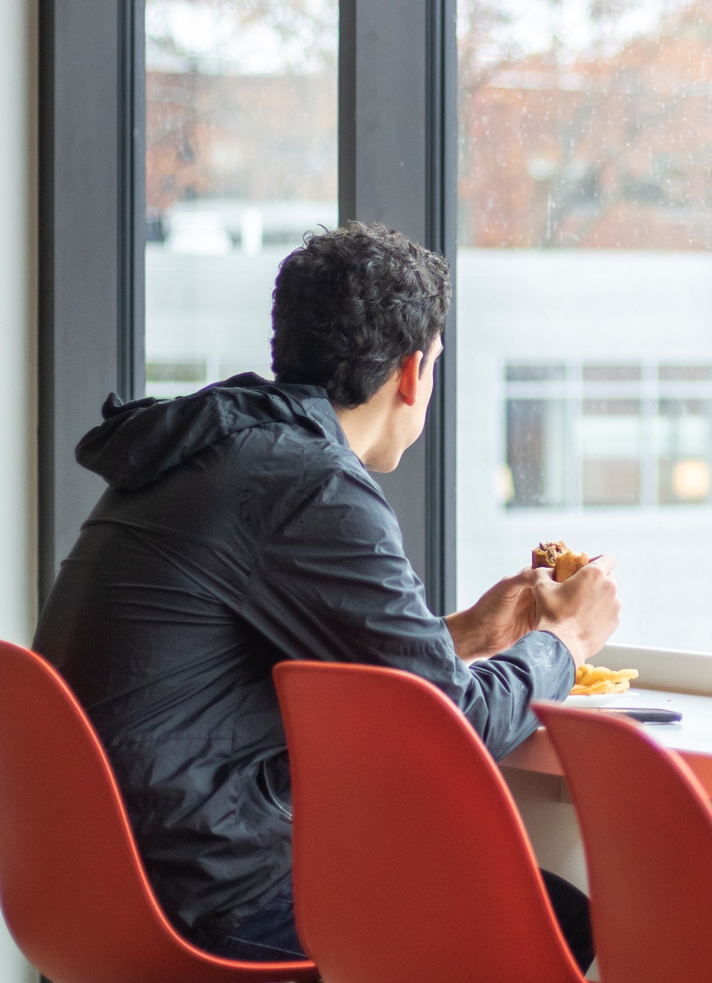 A student eating a hamburger while looking out large glass windows