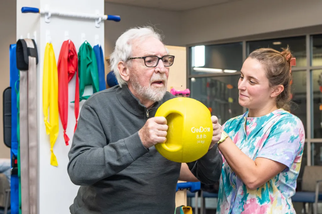 A previous D P T student assists a patient with arm exercises at their job