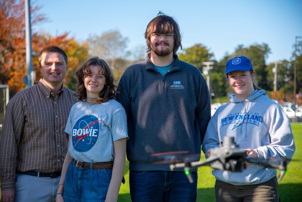 A faculty member and three students pose with a flying drone