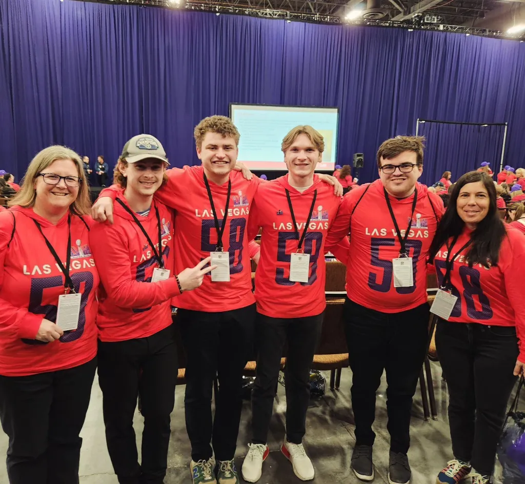 A group of students and faculty pose wearing Las Vegas-themed gear at the Super Bowl Experience