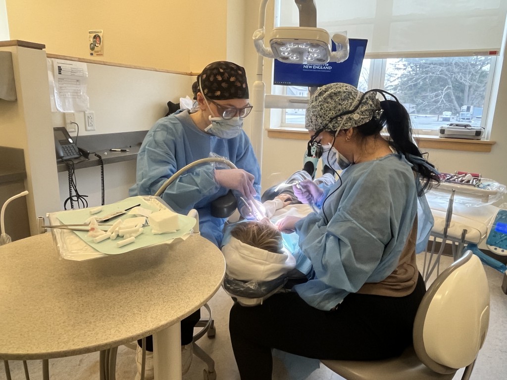 Two dental students clean a patient's teeth in the oral health clinic
