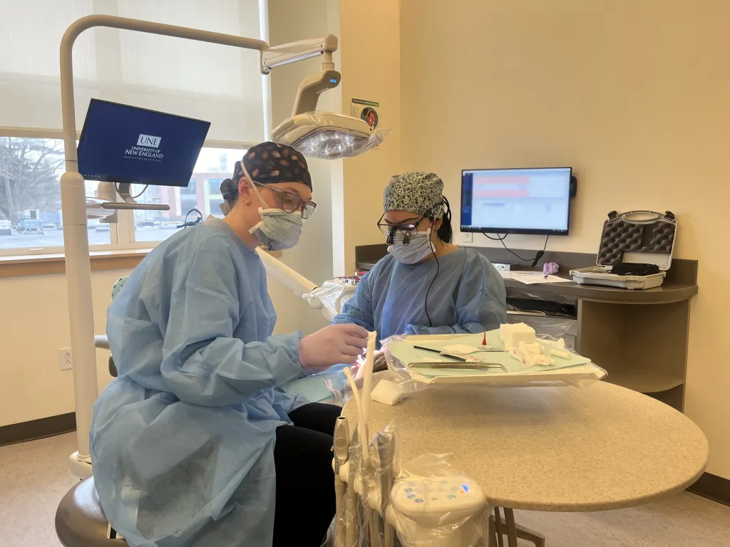 Two dental students clean a patient's teeth in the oral health clinic