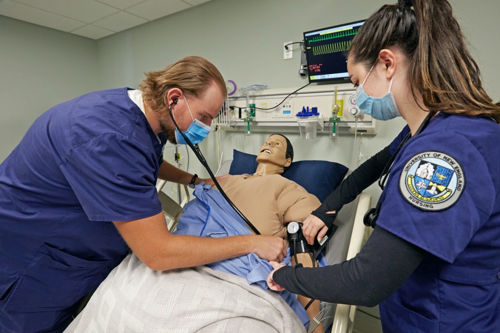 One A B S N student uses a stethoscope on a patient simulator as a fellow student watches