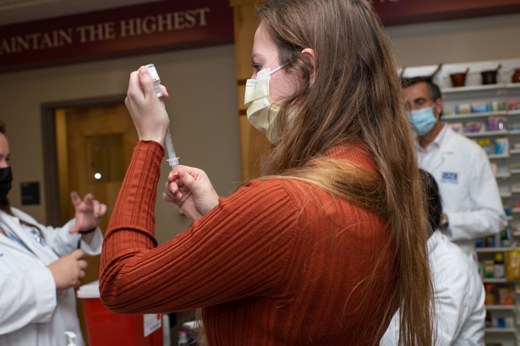 A pharmacy student preps a vaccine in a syringe