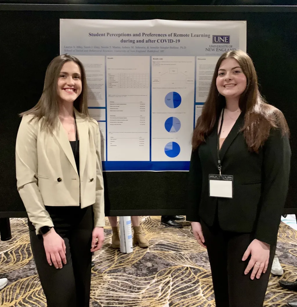 Two female students pose in front of a research poster