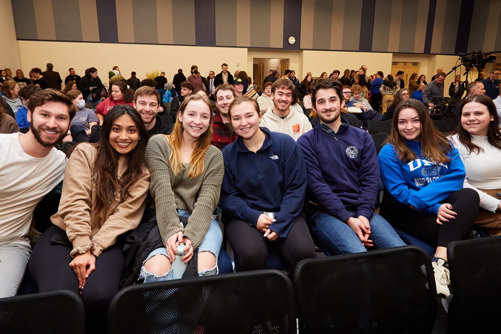 A group of U N E students sit in a row of the audience at a President's Forum