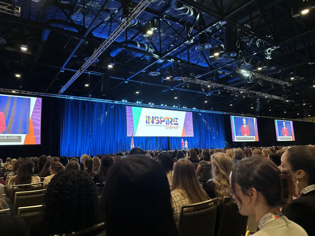 Large screens hang above a stage in the conference hall