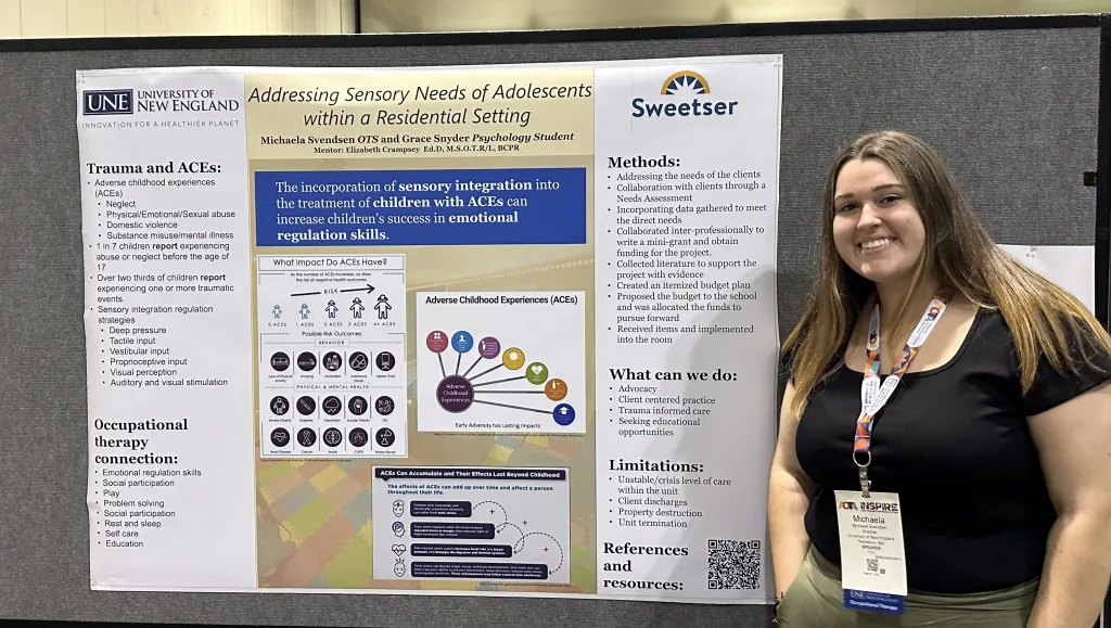 A UNE OT student poses in front of her research poster 