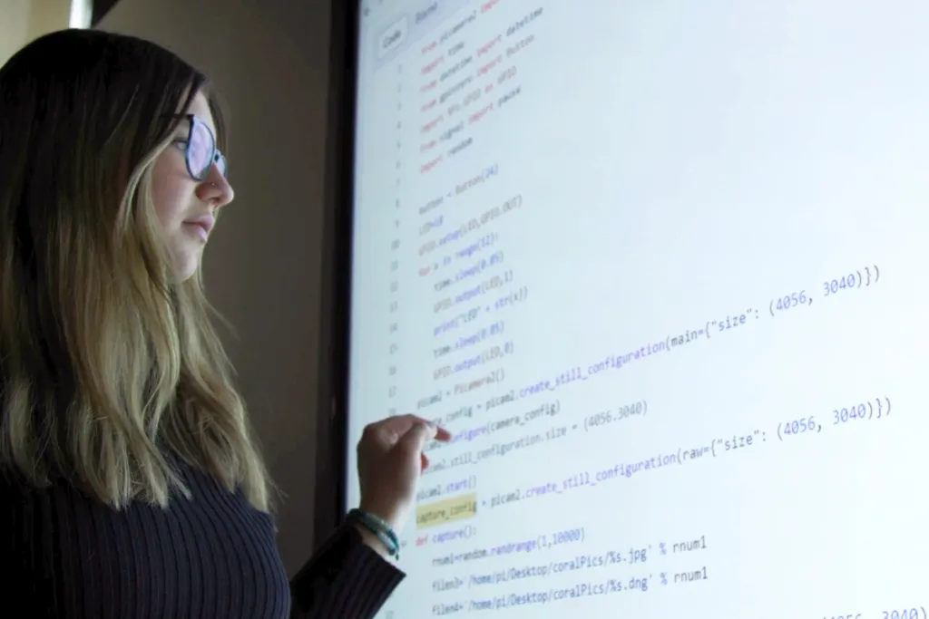 A computer science student reviews computer code on a large screen